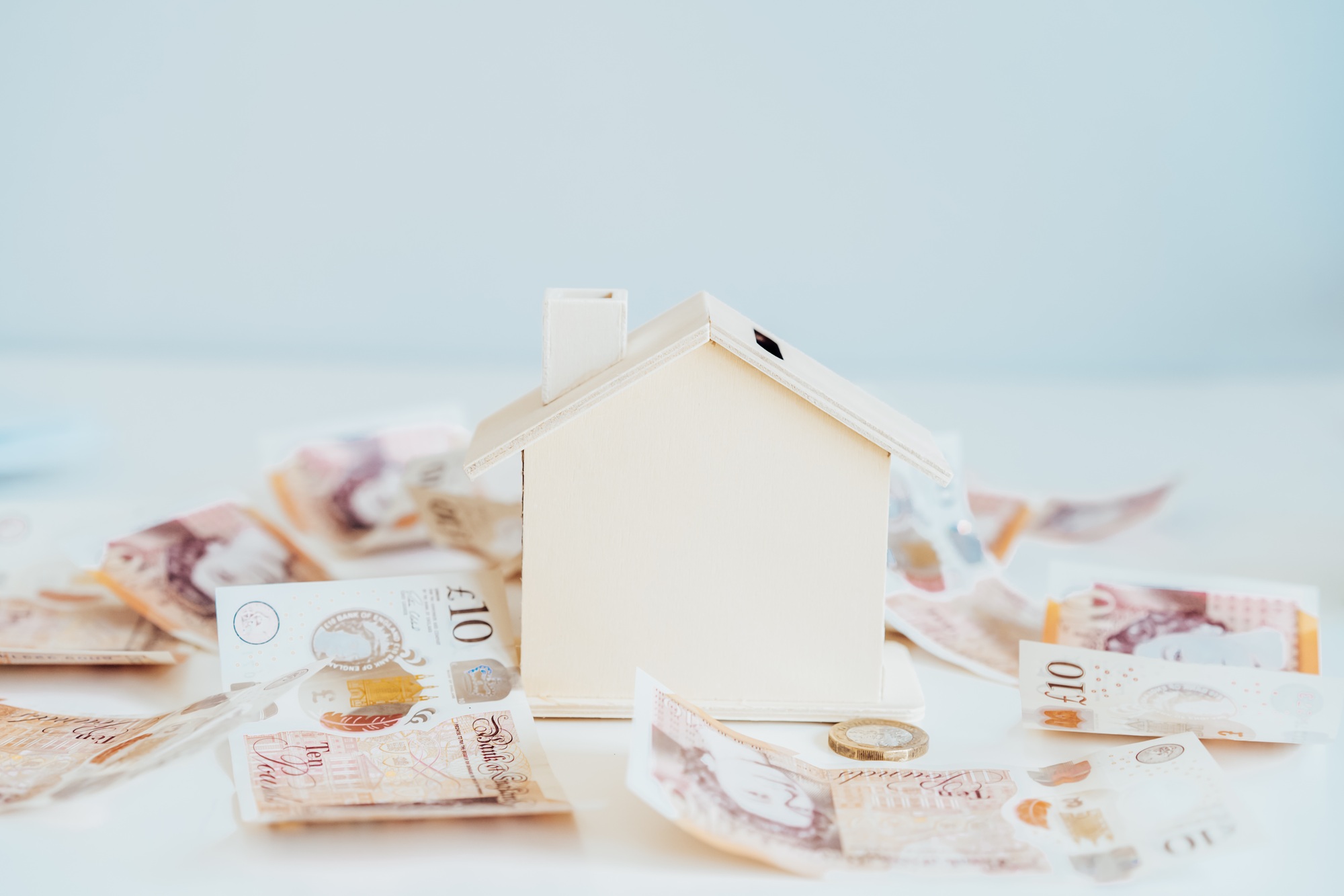 Wooden House model, piggy bank with British currency on the white table. Housing cost and payments.